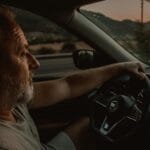 Starszy mężczyzna prowadzi samochód Nissan o zachodzie słońca