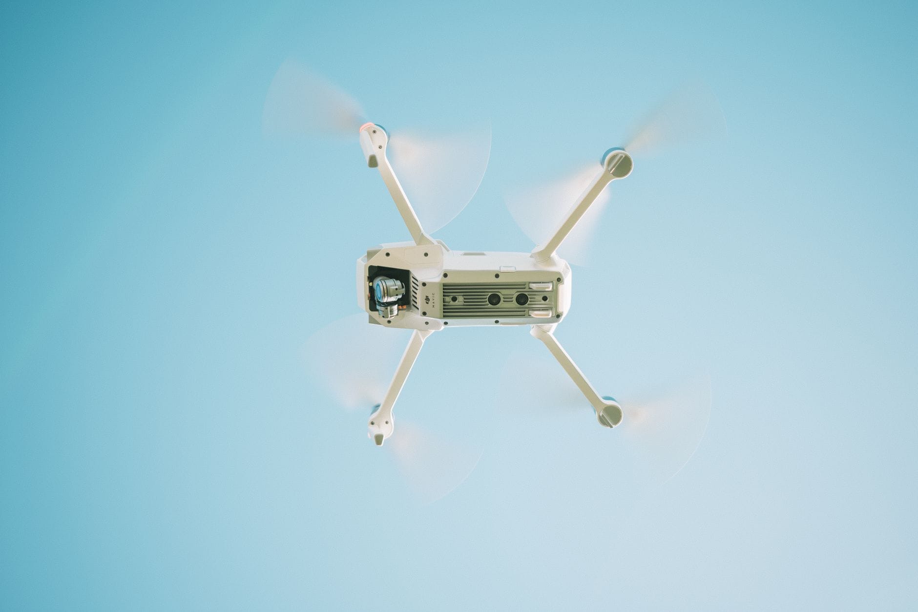 Biały dron w locie na tle bezchmurnego nieba, nagrywa ujęcia z góry