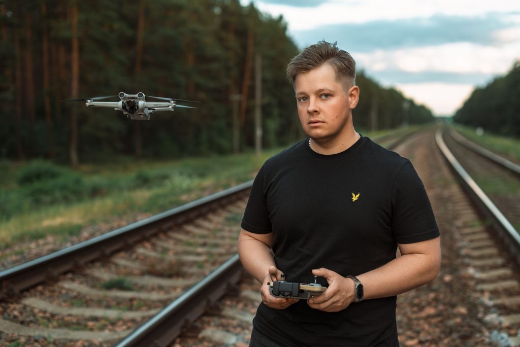 Mężczyzna steruje dronem na torach kolejowych w leśnej scenerii